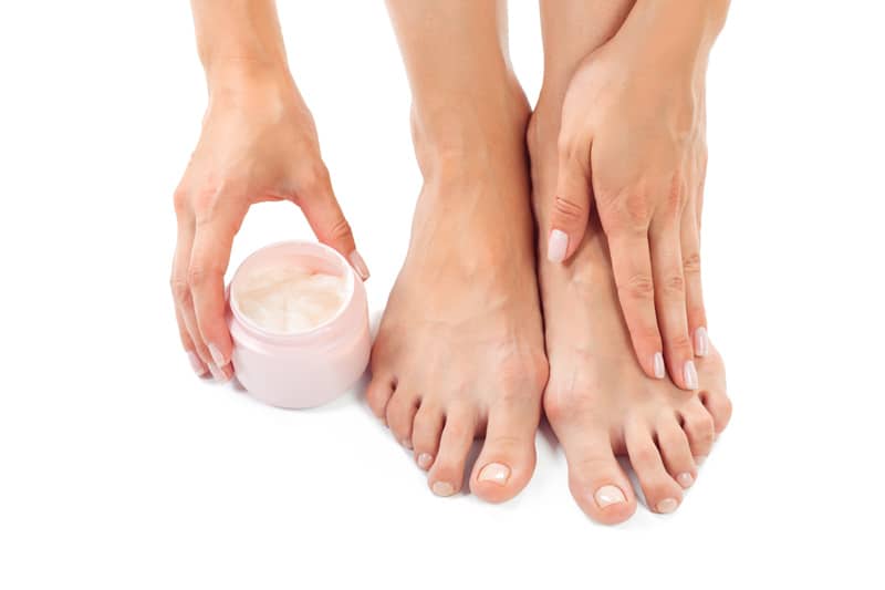 manos de mujer colocándose crema en los pies